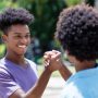 African american young adult man gives high five to friend with afro hair outdoor in summer in city